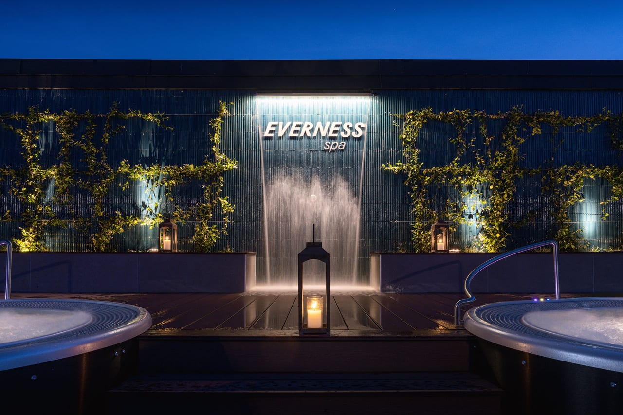 Spa Everness en nocturne — mur d'eau illuminé, bougies et jacuzzis