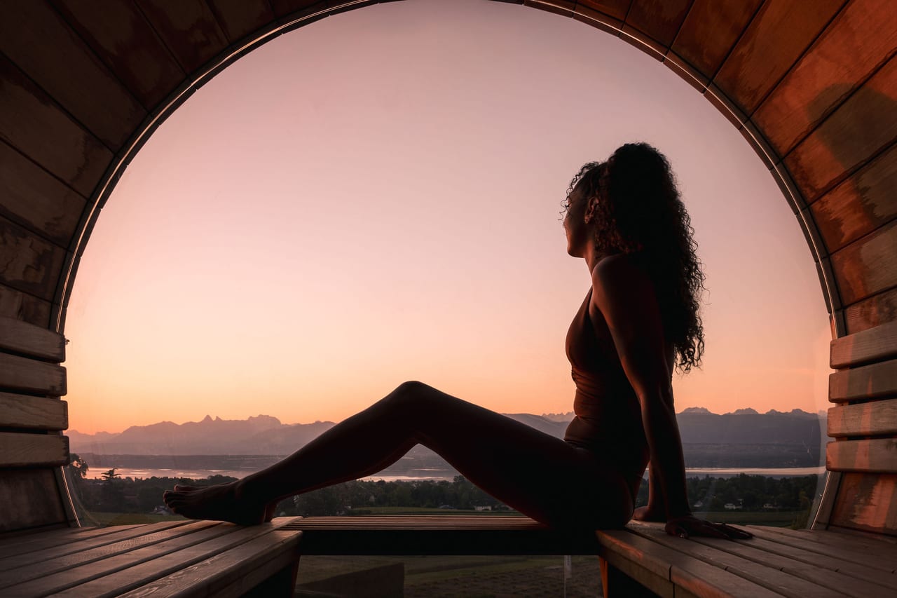 Silhouette dans le sauna tonneau panoramique Everness face aux Alpes au coucher de soleil